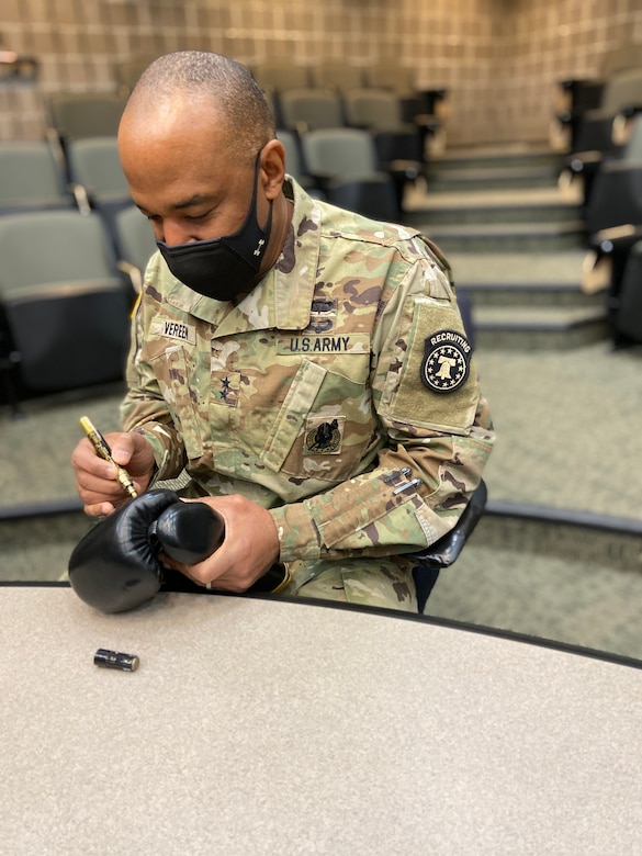 An Army soldier signing a boxing glove with a pen.