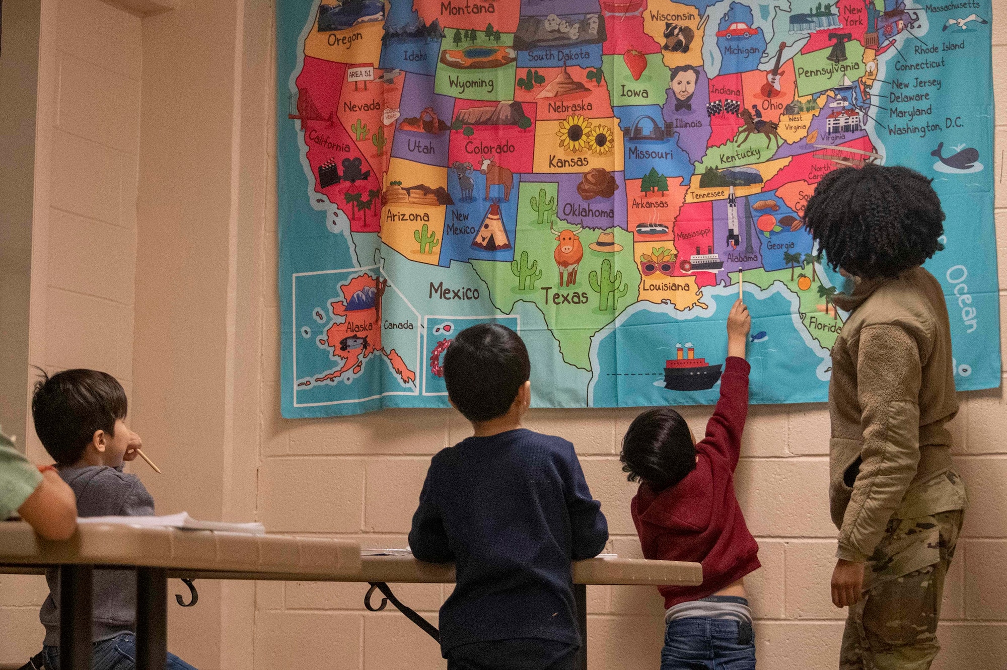 U.S. Air Force Senior Airman Cicely McWhorter, Task Force-Liberty Joint Readiness Center floor operations, teaches Afghan children the names of the 50 states in Liberty Village on Joint Base McGuire-Dix-Lakehurst, New Jersey, Feb. 1, 2022. The Department of Defense, through U.S. Northern Command, and in support of the Department of Homeland Security, is providing transportation, temporary housing, medical screening, and general support for at least 11,000 Afghan evacuees at Liberty Village, in permanent or temporary structures, as quickly as possible. This initiative provides Afghan personnel essential support at secure locations outside Afghanistan.