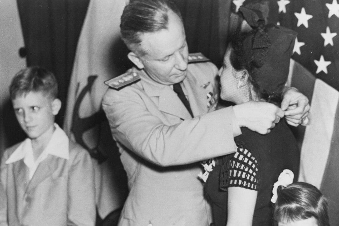 A man puts a medal around a woman's neck. Two small children stand beside them.