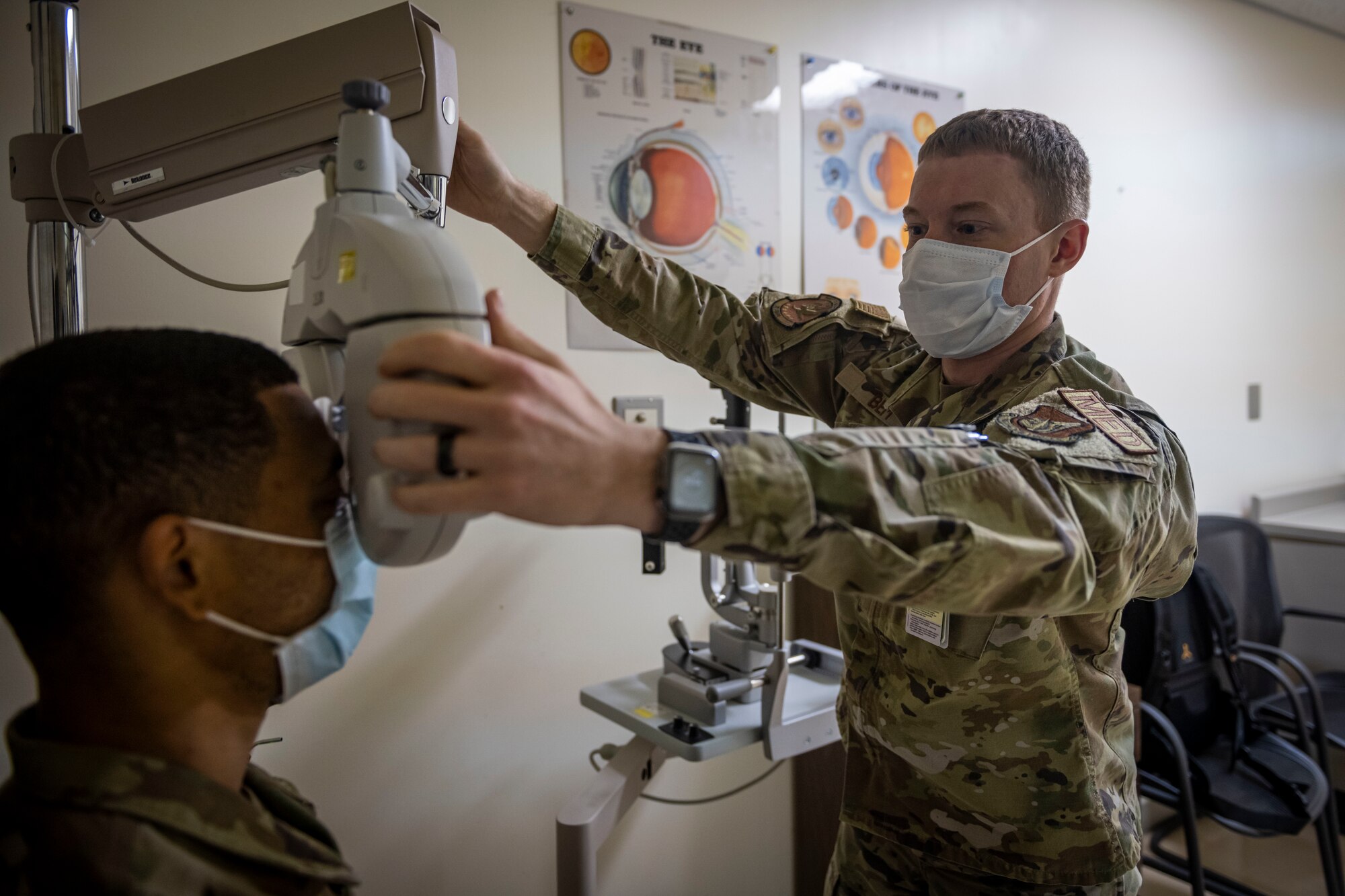 Man in military uniform looks through medical instrument to examine a patient's eyes.