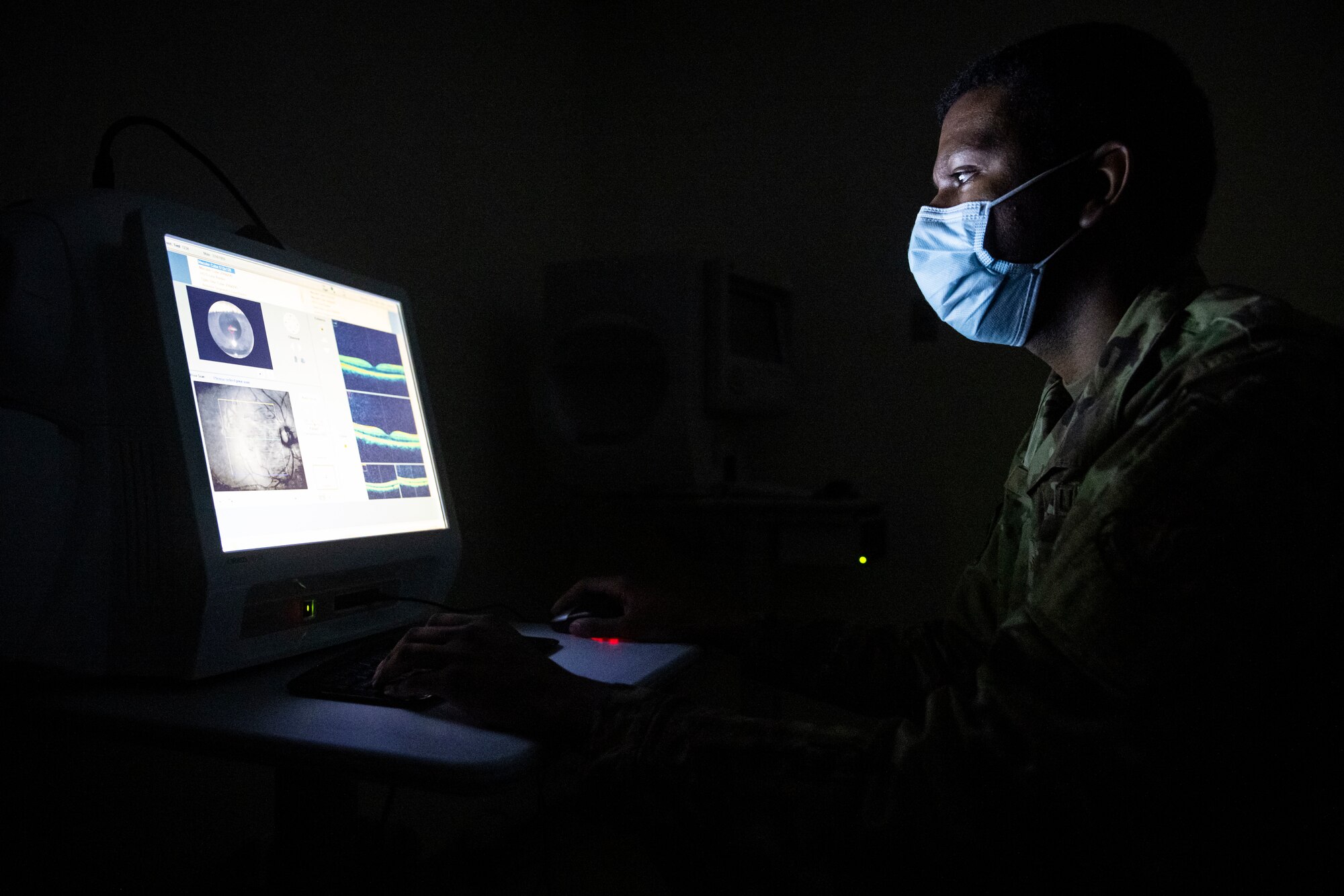 Man in military uniform looks at a computer monitor in a dark room.