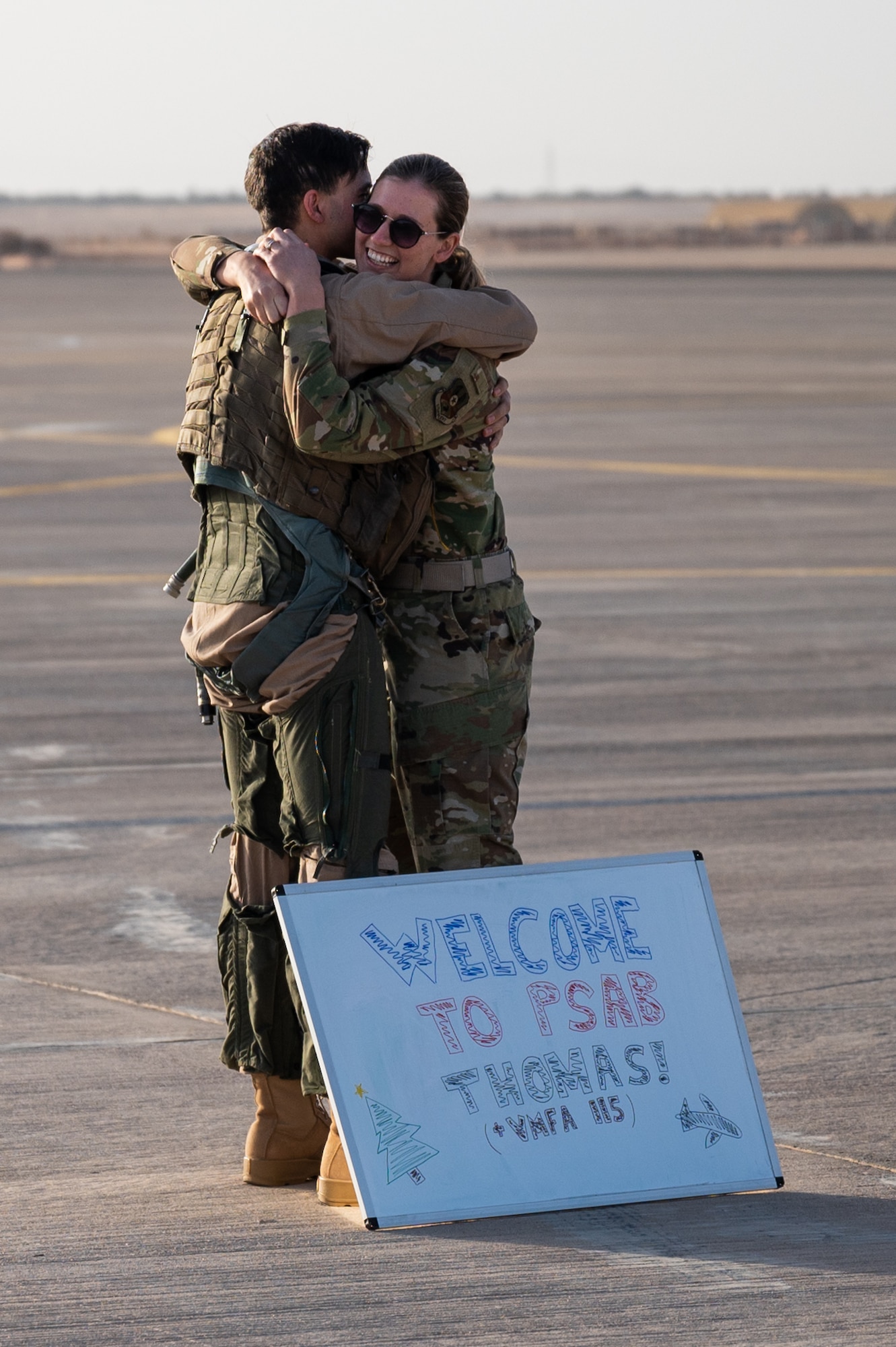 U.S. Marine Capt. Thomas Phillips, Marine Fighter Attack Squadron 115 weapon systems officer, hugs his wife U.S. Air Force 1st Lt. Alyson Phillips, 378th Expeditionary Contracting Squadron infrastructure flight commander, Dec. 23, 2021, at Prince Sultan Air Base, Kingdom of Saudi Arabia. The couple reunited after Thomas' unit deployed PSAB, where Alyson was already deployed. (U.S. Air Force photo by Senior Airman Jacob B. Wrightsman)