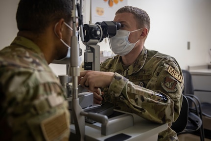 Man in military uniform looks through medical instrument to examine a patient's eyes.