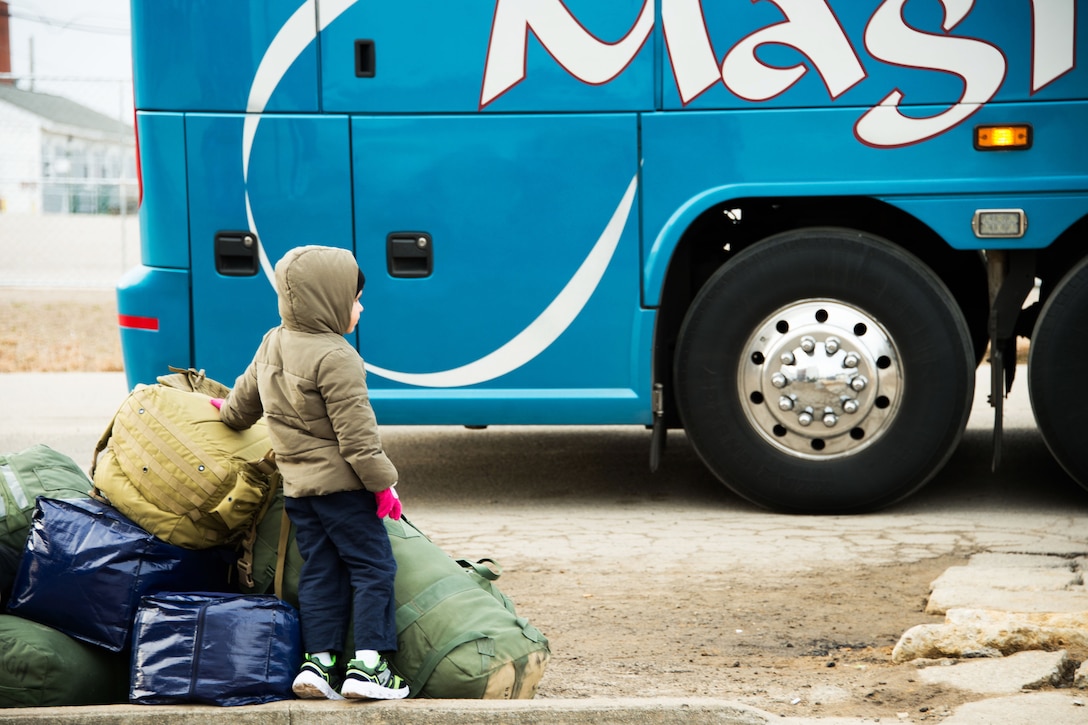 A little boy wearing a face mask waits to board a bus.