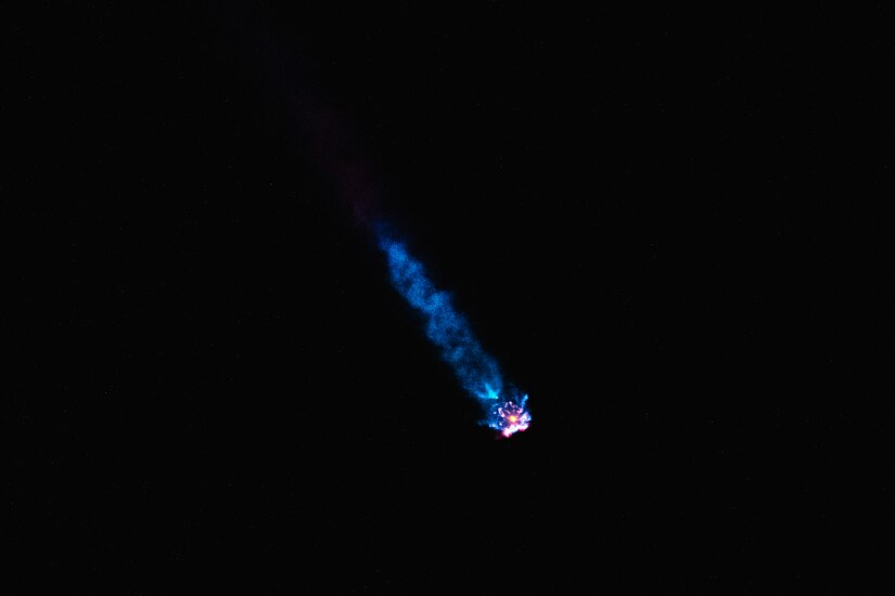 A rockets gives off a blue light while traveling through dark space.