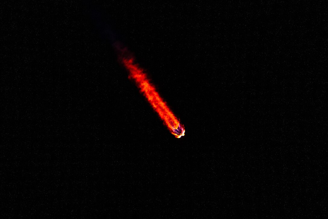 A rocket travels through the darkness giving off a red light.