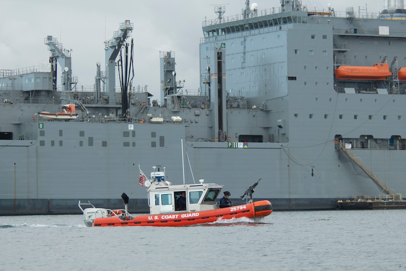 A small boat moves in front of a large military ship.
