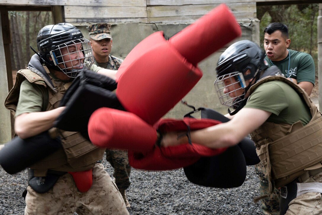 Two Marine Corps recruits fight using rubber batons during training as fellow service member watch.