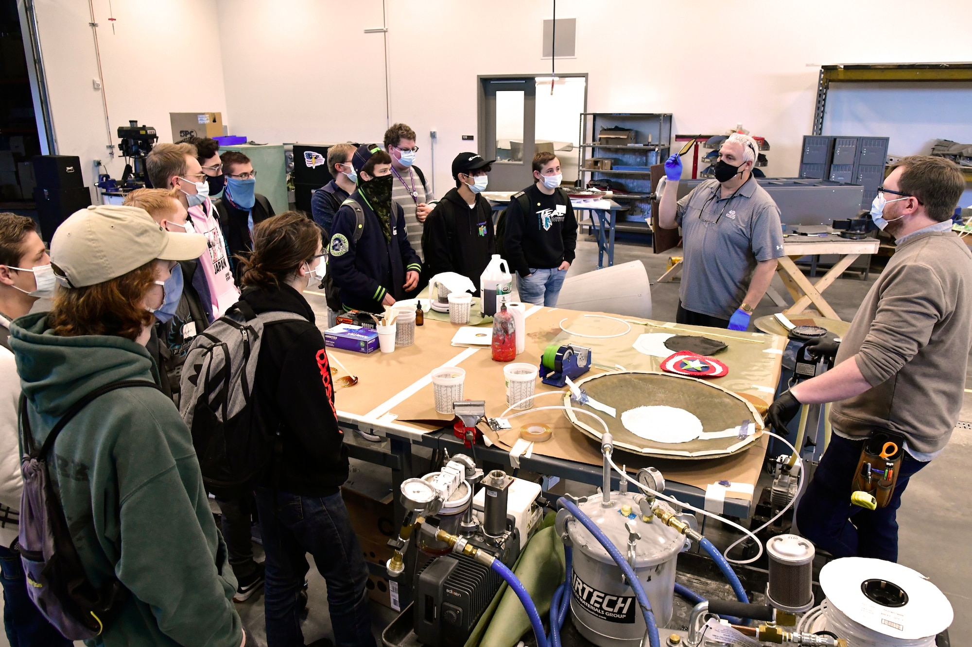 High school students stand around a table littered with tools and other materials inside the museum's aircraft renovation center.