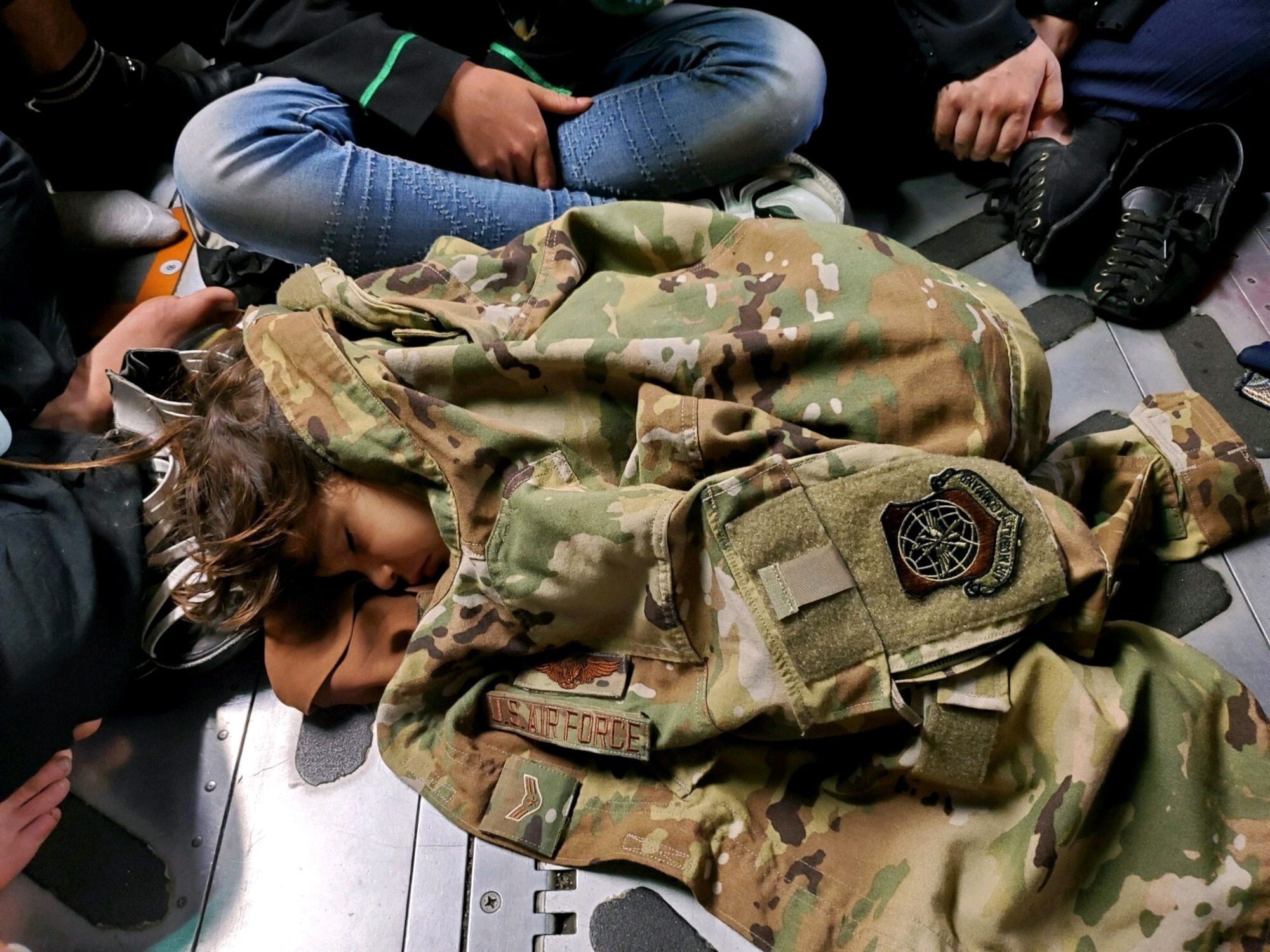 Refugee child lays on ground with military jacket blanket