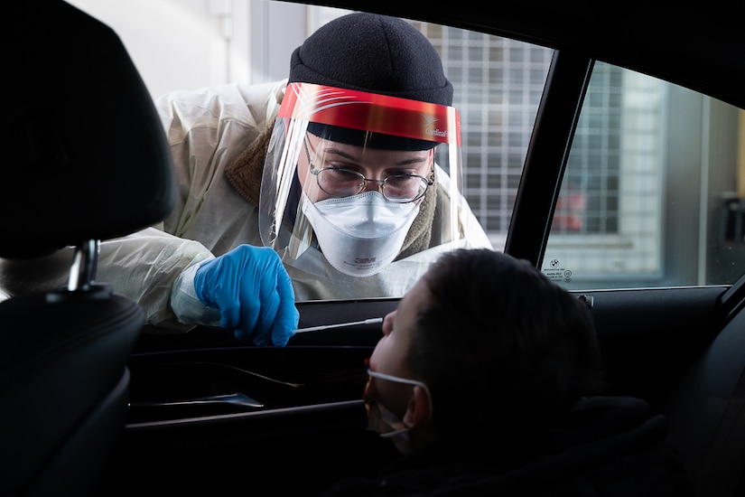 A man leans through a car window to swab the nose of a young boy.