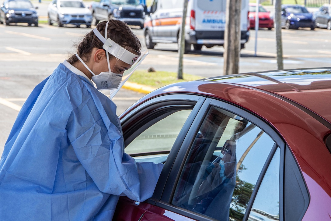 A soldier wearing personal protective equipment holds a nasal swab while administering a COVID-19 test.