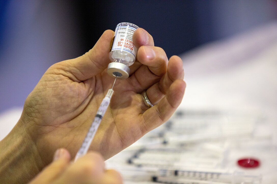 A person holds a syringe while inserting it into a vial.