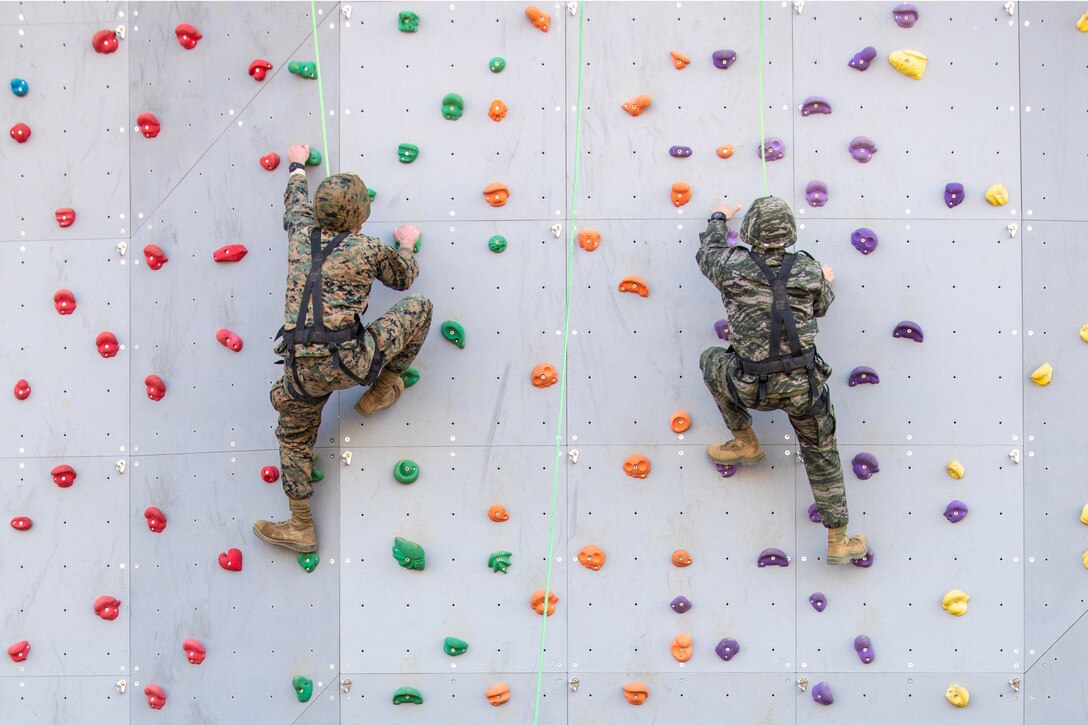 A Marine and a foreign service member climb a rock wall.