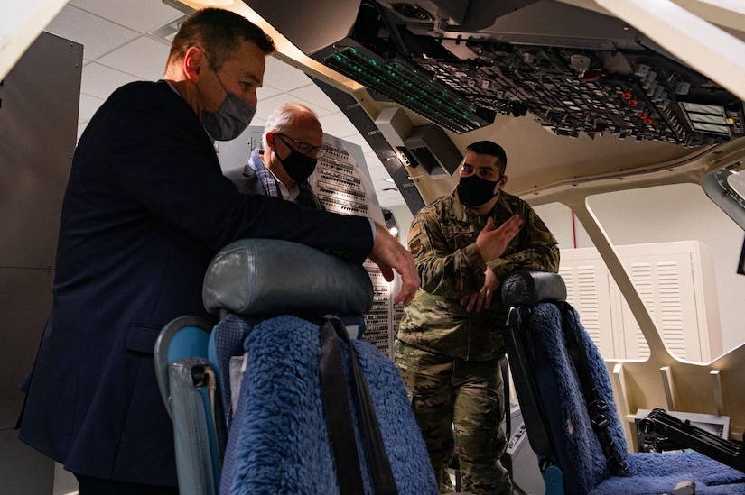 Three men observe a C-17 training simulator