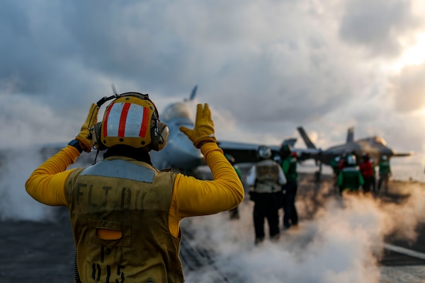 A Sailor directs an F/A-18E Super Hornet on the flight deck of the Nimitz-class aircraft carrier USS Abraham Lincoln (CVN 72).