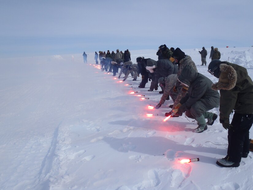 Airmen in a line place flares in a snowy field.