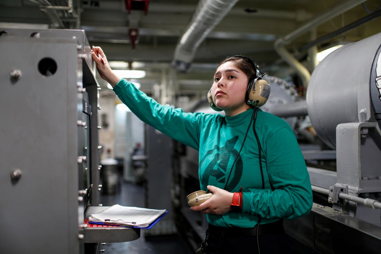 A sailor with headset and microphone looks up.