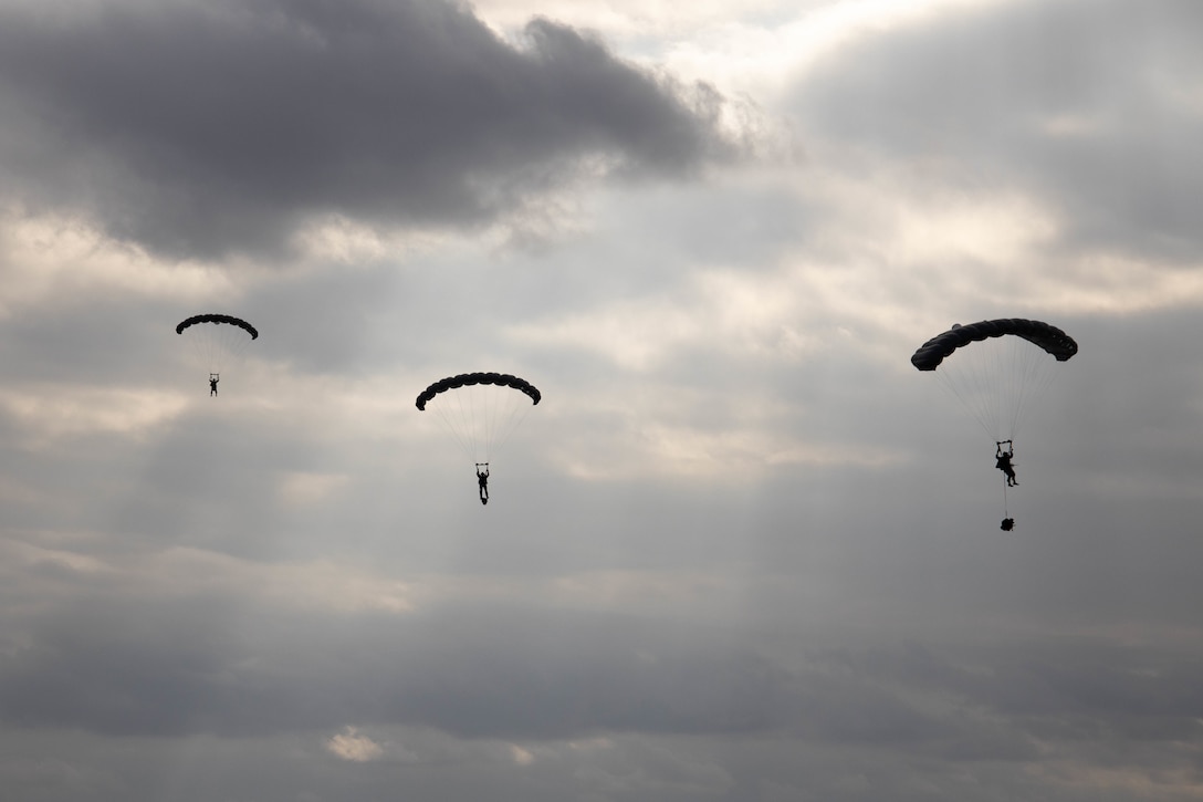 Three Marines parachute downwards as the sun breaks through the clouds.