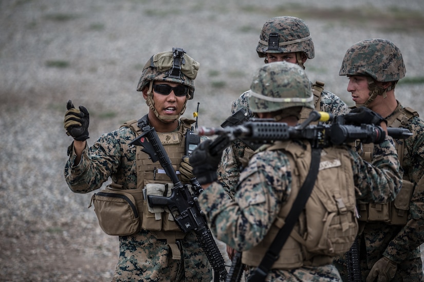 Four Marines in combat gear stand together in a group outdoors.