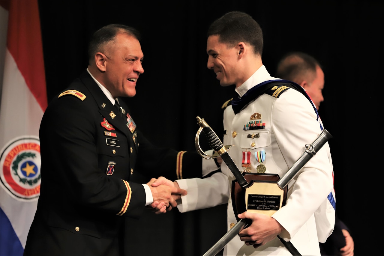 Two male service members shake hands.