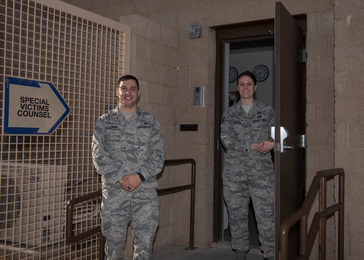 Two airmen pose for a photo just outside a doorway.