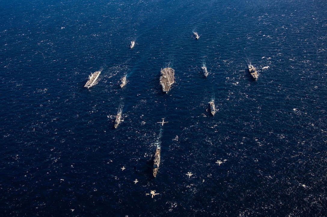 Aircraft fly over ships transiting a body of water.