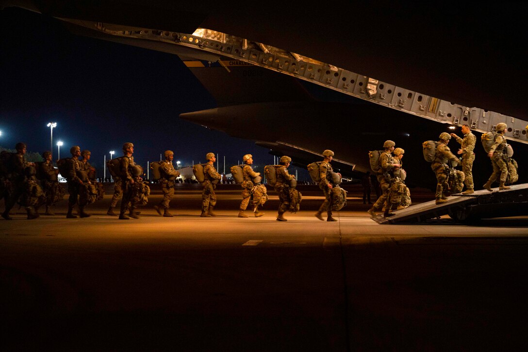 A line of soldiers board the back of an aircraft.