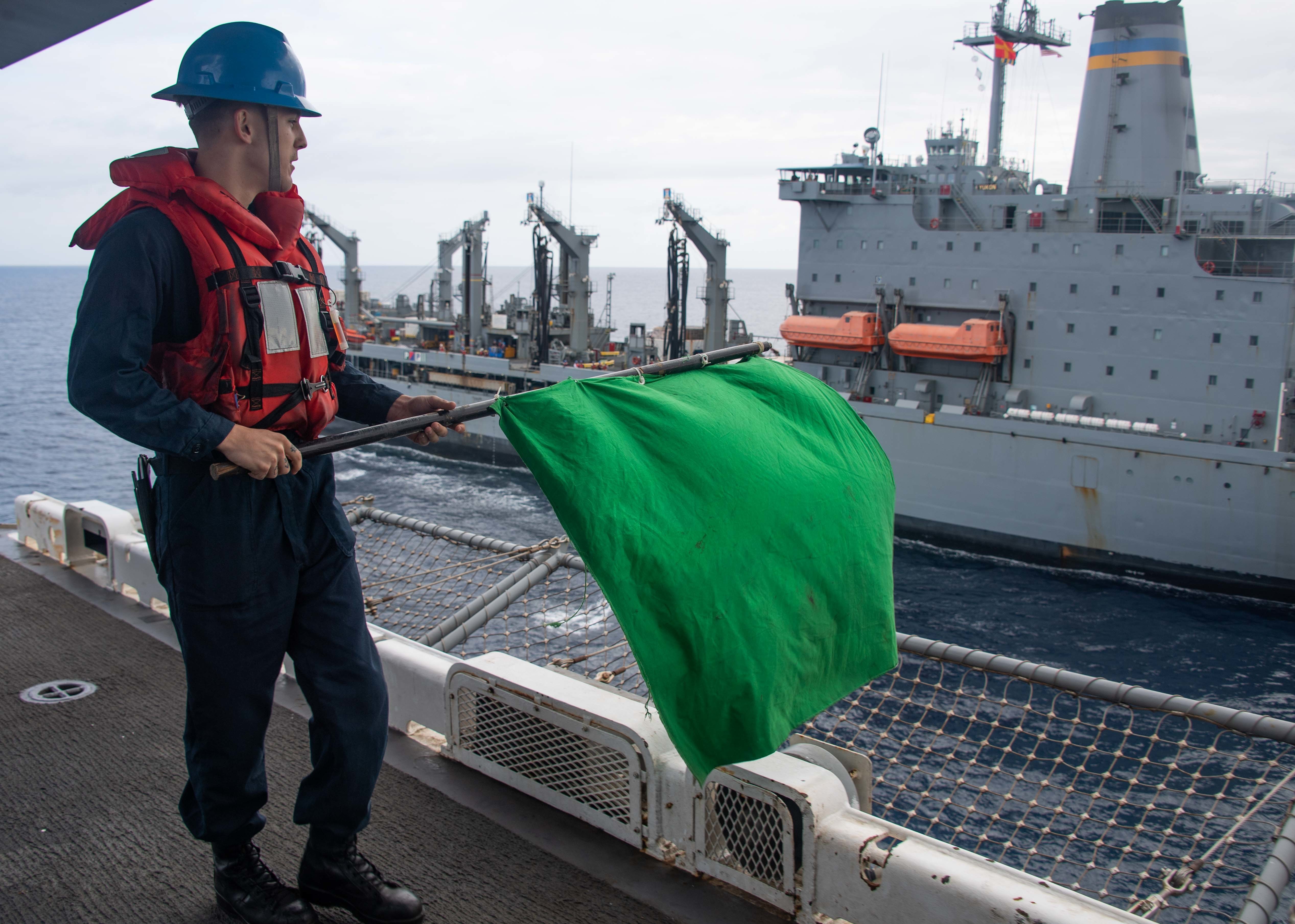A Sailor signals to the military Sealift Command fleet replenishment oiler USNS Yukon (T-AO 202) aboard Essex during a replenishment-at-sea in support of Noble Fusion, Feb. 4, 2022.