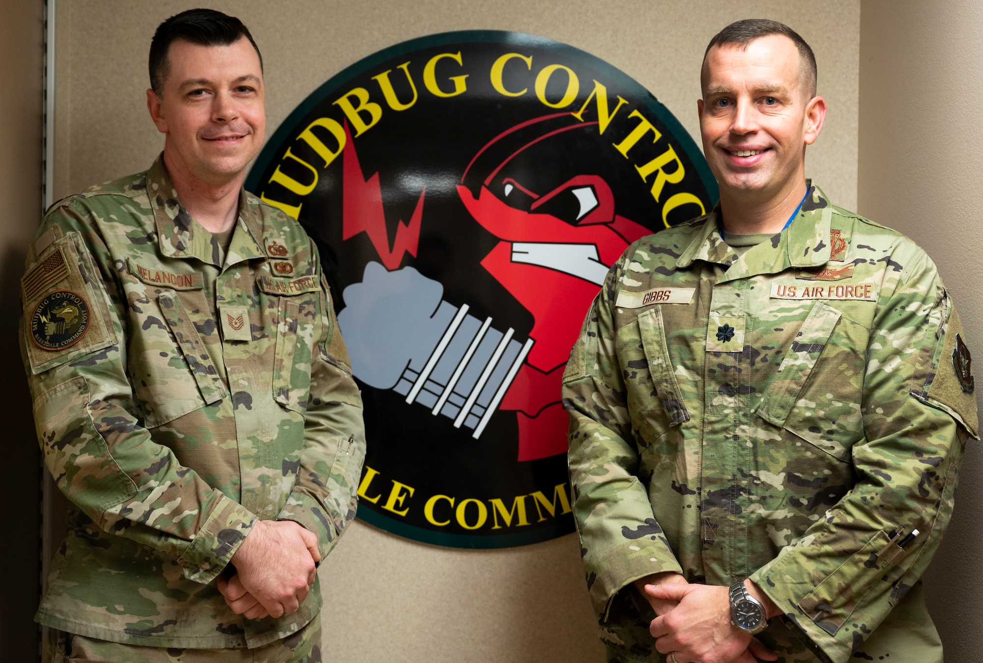 Two Airmen stand in from of a sign.