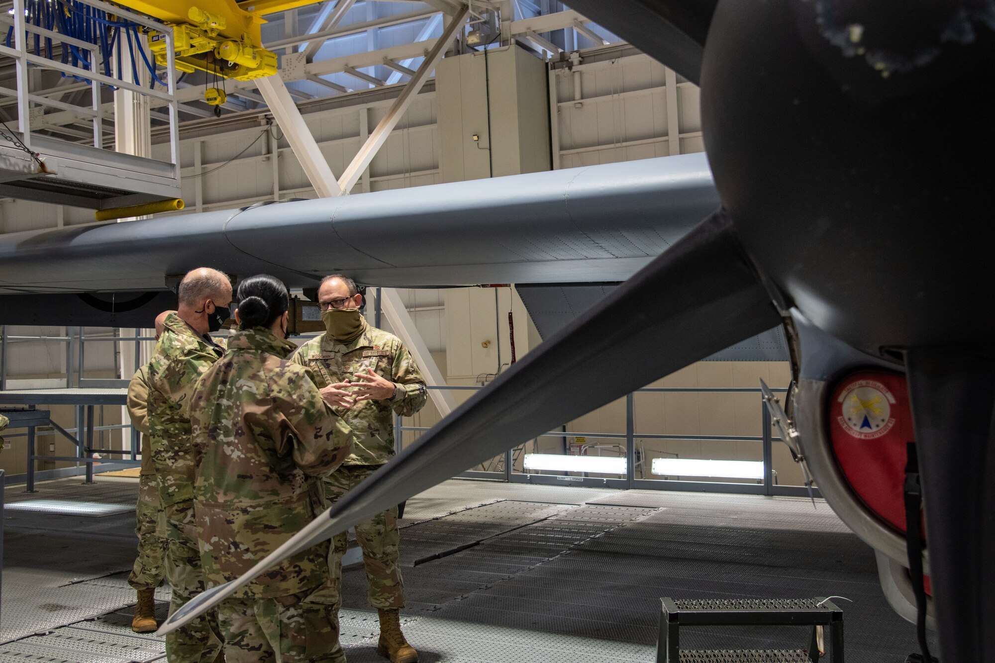 Three uniformed Airmen stand to the left with a C-130J wing in the background and propellor in the foreground