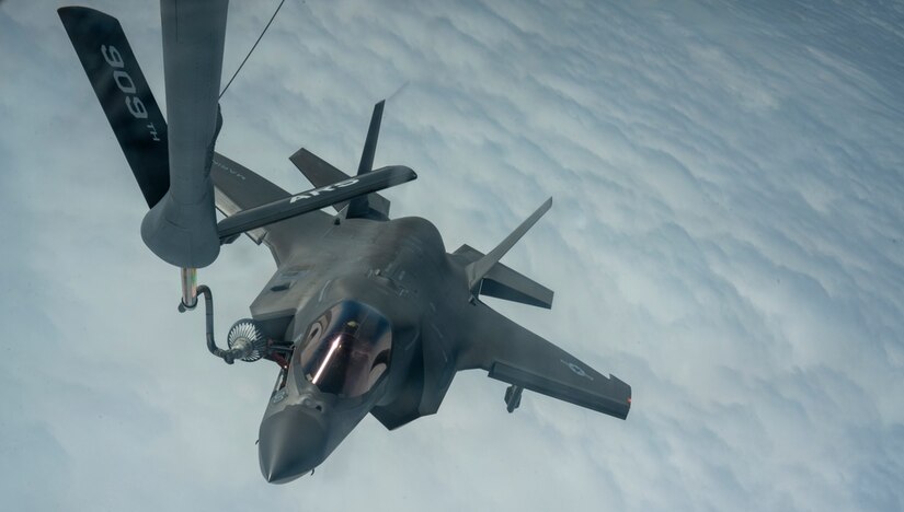 A Marine Corps F-35B Lightning II aircraft receives fuel from another plane while in flight over clouds.