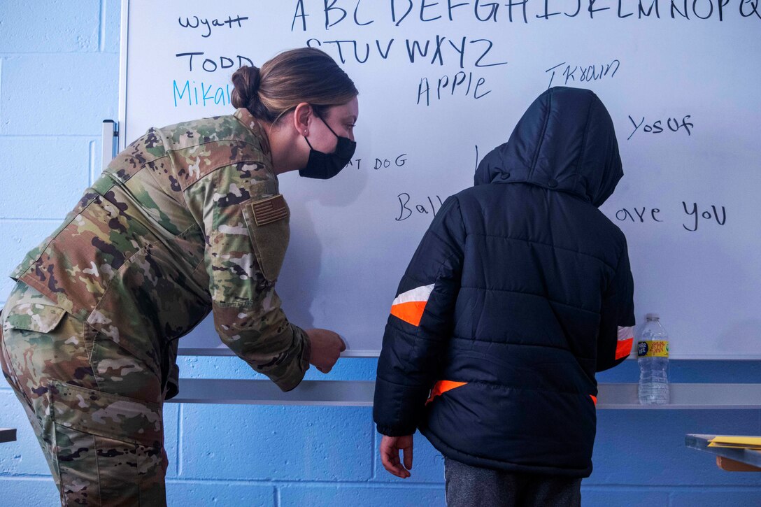 A soldier wearing a face mask teaches English to an Afghan child.