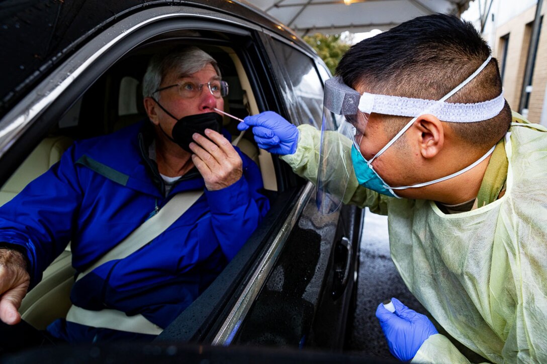 An airman wearing personal protective equipment holds a nasal swab to administer a COVID-19 test.