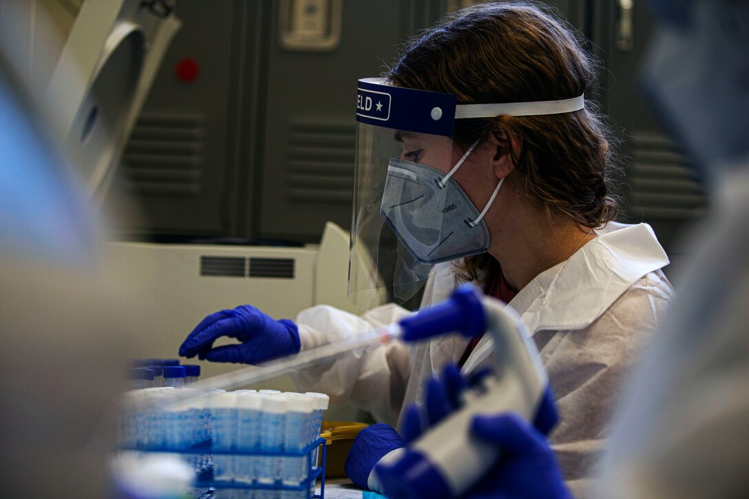 A woman wearing personal protective equipment processes laboratory specimens.