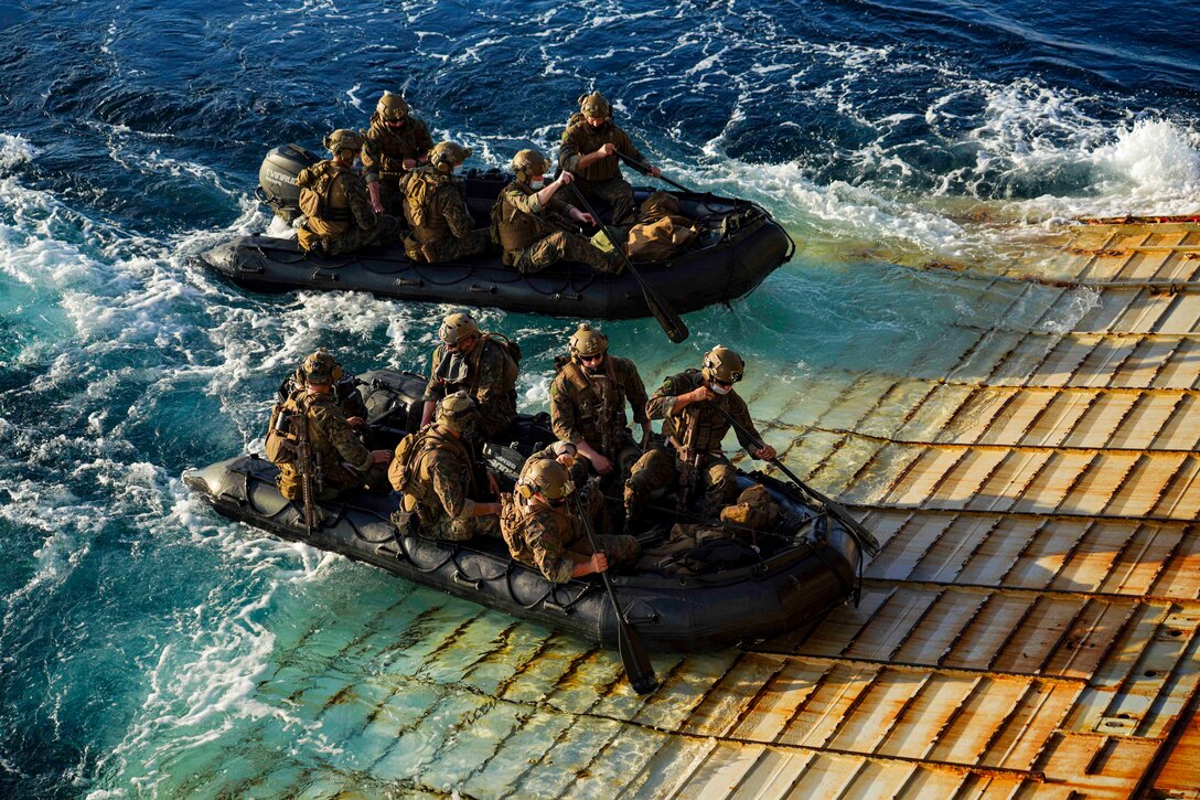 Marines ride in inflatable boats toward the gate of a ship.