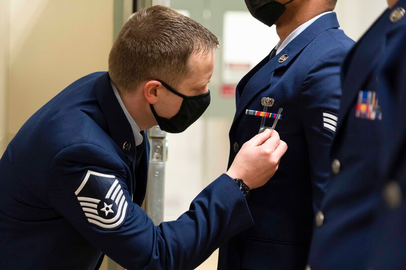 A airman uses a tool to measure another airman's uniform.