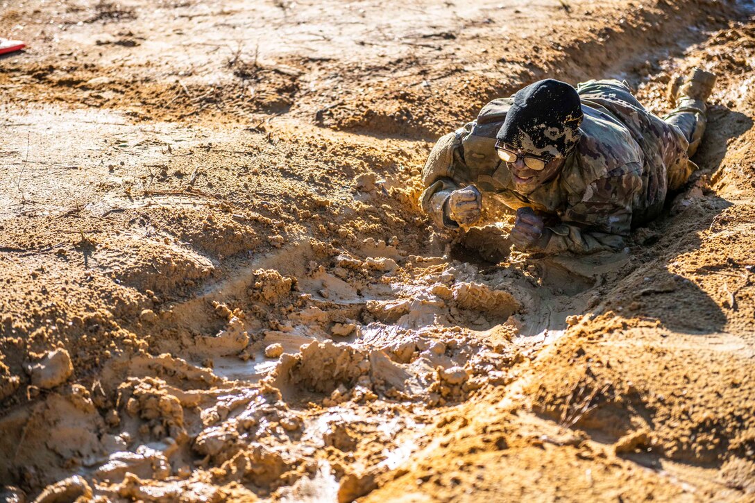 A soldier crawls through muddy sand.