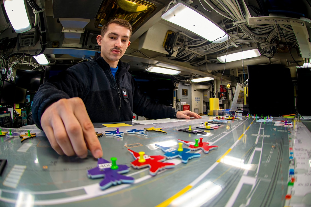 A sailor moves figures on a board aboard a ship at sea.