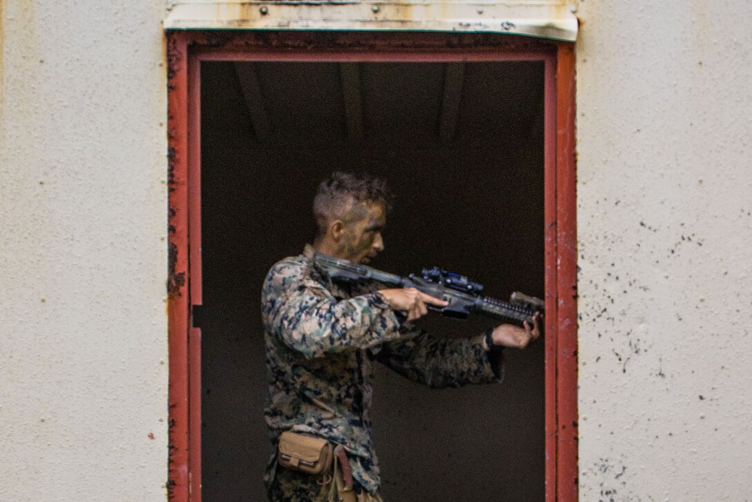 A Marine enters a building with rifle aimed.