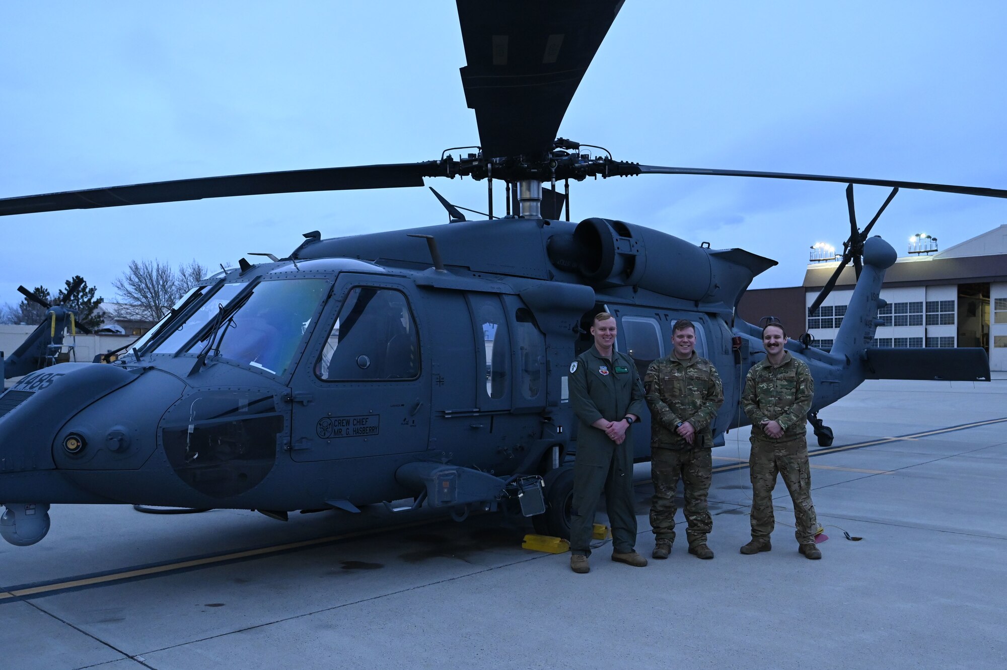 Three men stand in front of a helicopter.
