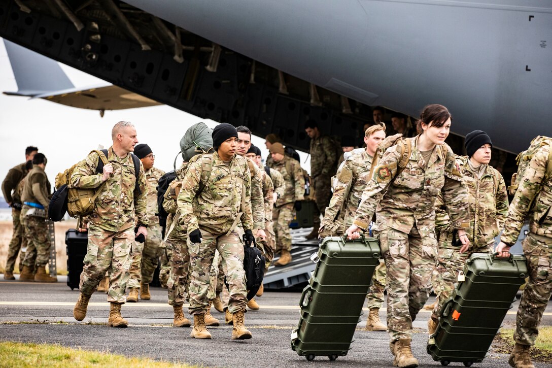 Soldiers depart a military aircraft.