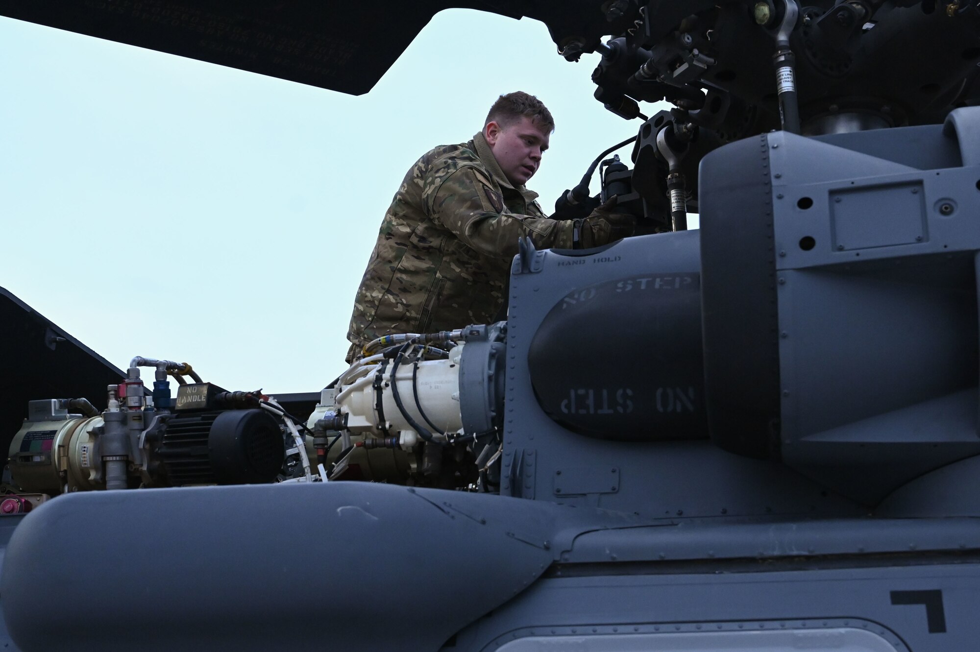 A man checks rotors on top of a helicopter.