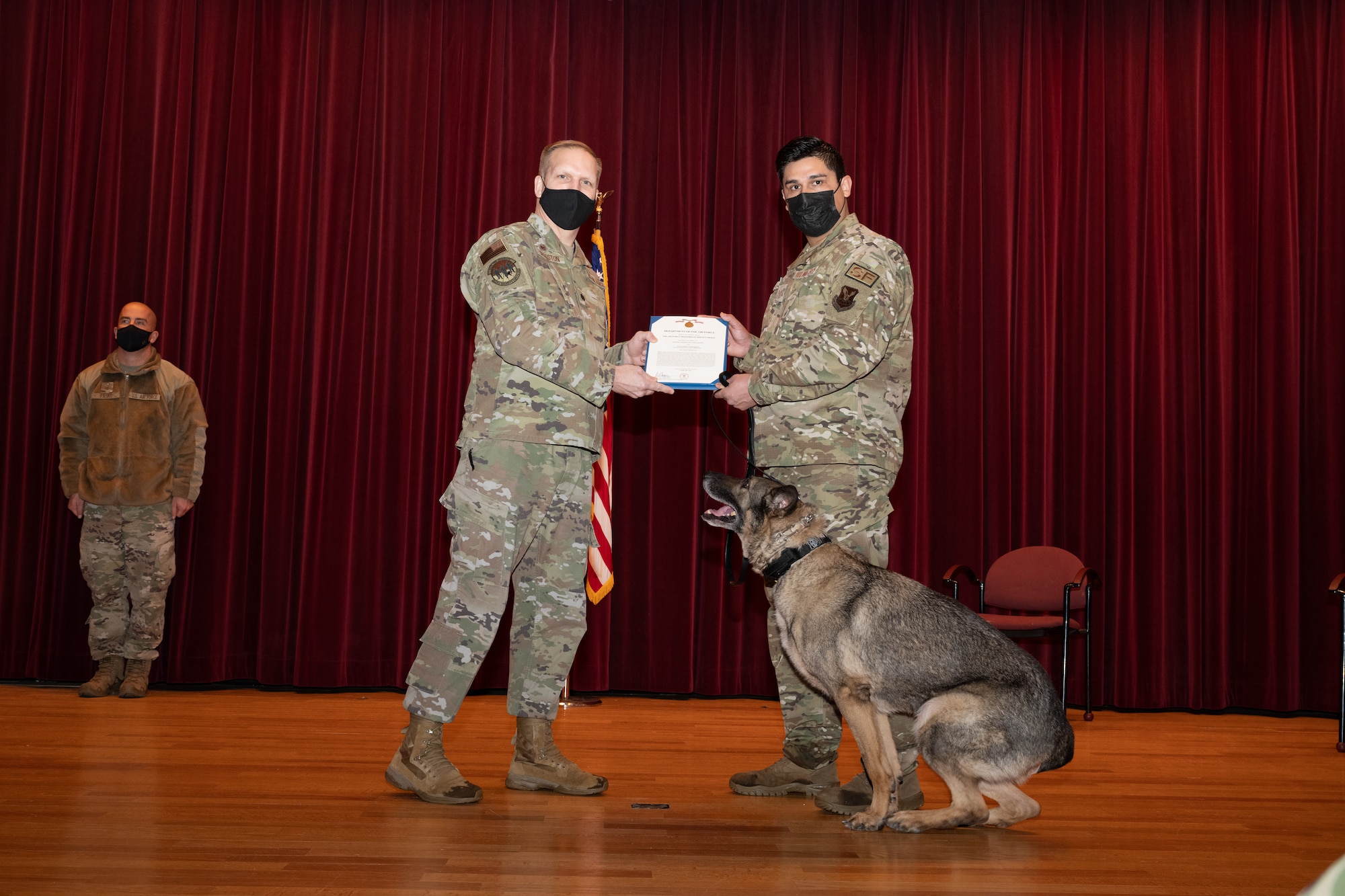 U.S. Air Force Lt. Col. Sproston, 509th Security Forces Squadron Commander, presents U.S. Air Force Staff Sgt. Alex Villalpando, 509th Security Forces military working dog handler, with U.S. Air Force MWD Stiffler's Meritorious Service Medal certificate during Stiffler's retirement ceremony at the base theater on Whiteman Air Force Base Feb. 4, 2022. Military working dogs provide a valuable force multiplier to aid in the security and readiness within our units. (U.S. Air Force photo by Airman 1st Class Bryson Britt)
