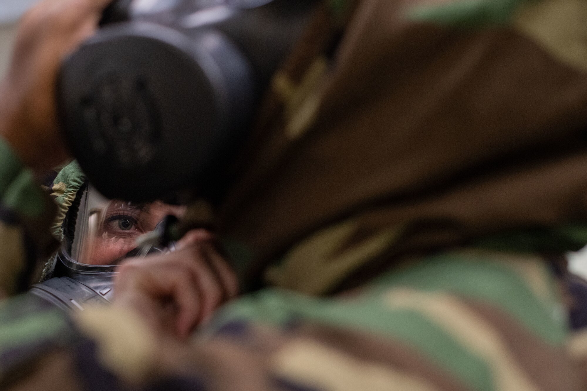 An Airman in full MOPP gear adjusts the hood of a person in the foreground