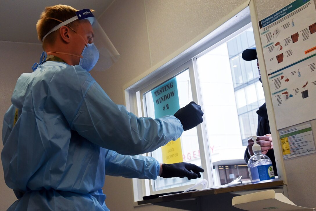 An airman wearing personal protective equipment helps someone with a COVID-19 test.