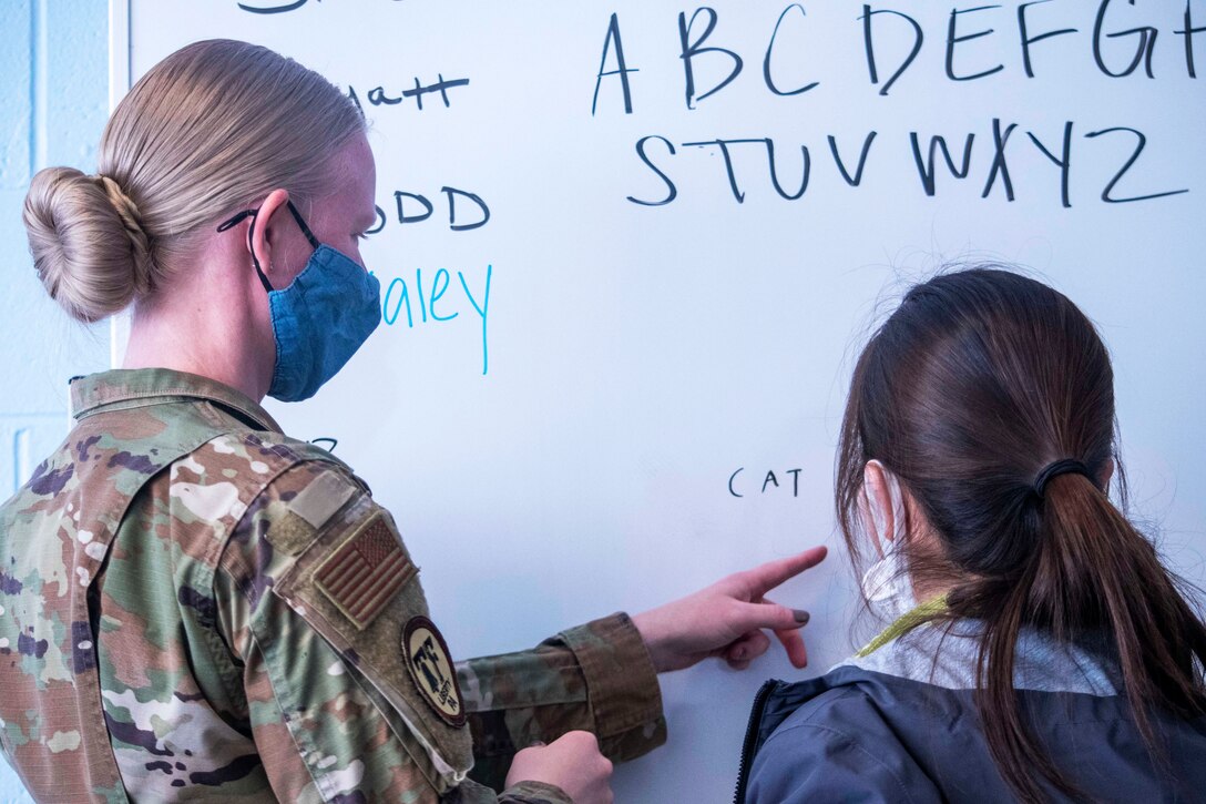 A soldier wearing a face mask teaches English to an Afghan child.