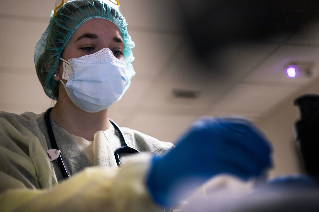 A woman wearing a face mask, gloves, medical gown, surgical cap and a stethoscope around her neck updates a patient’s medical chart