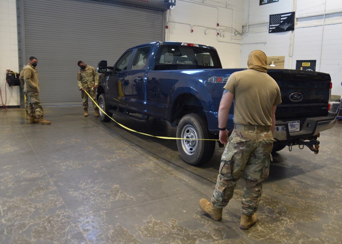 Two Airman hold a tape measurer the length of a blue pickup truck while an Airman to the left watches