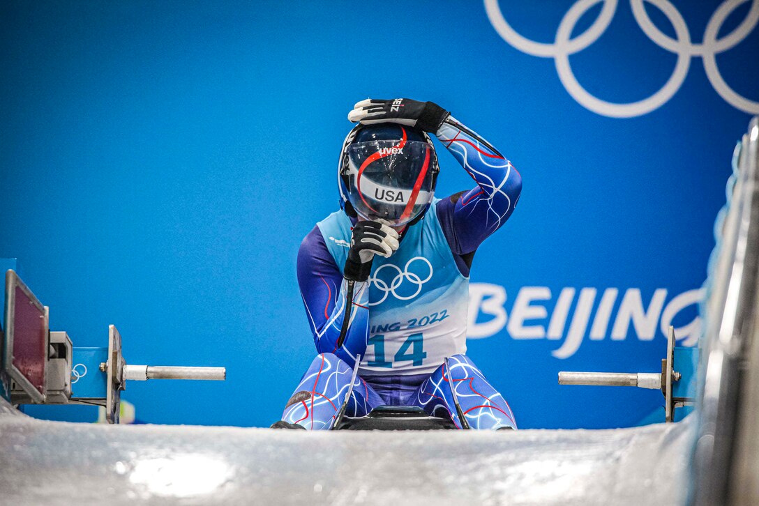 A soldier adjusts her helmet while sitting on a sled.